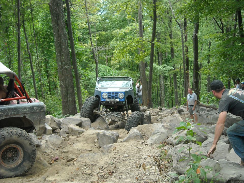 Blue Ford Bronco crawling over rocks in a forest