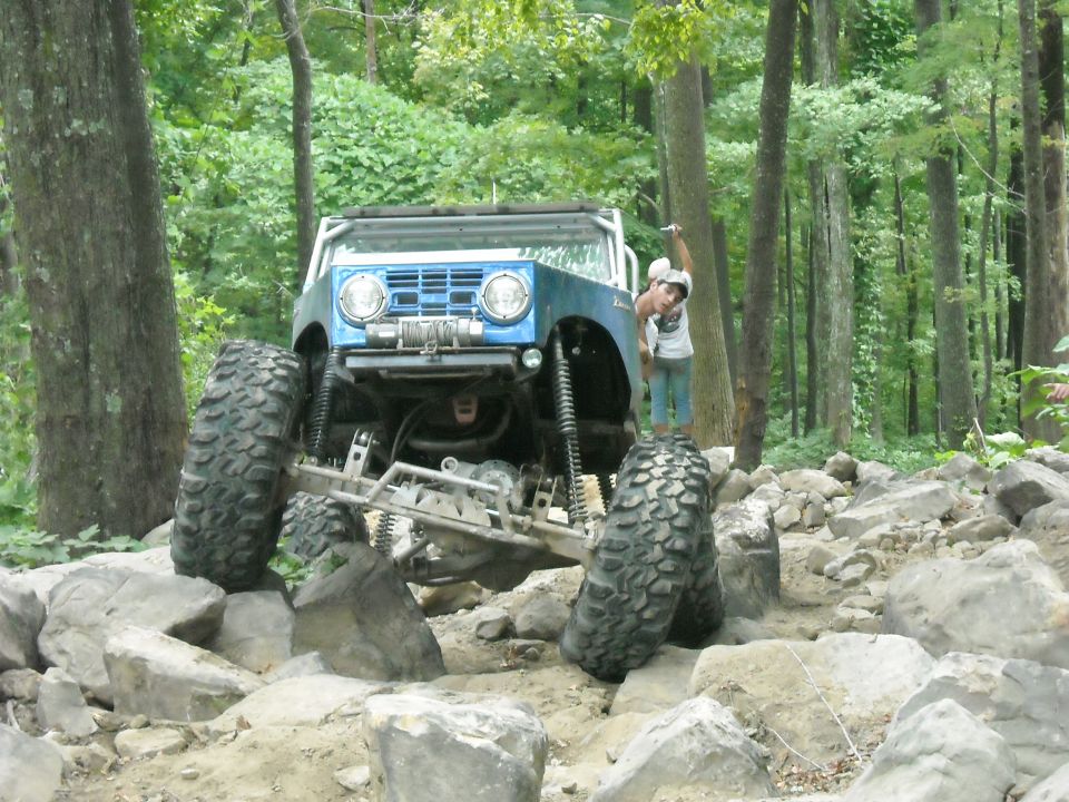 Blue Ford Bronco flexing over boulders with spotter