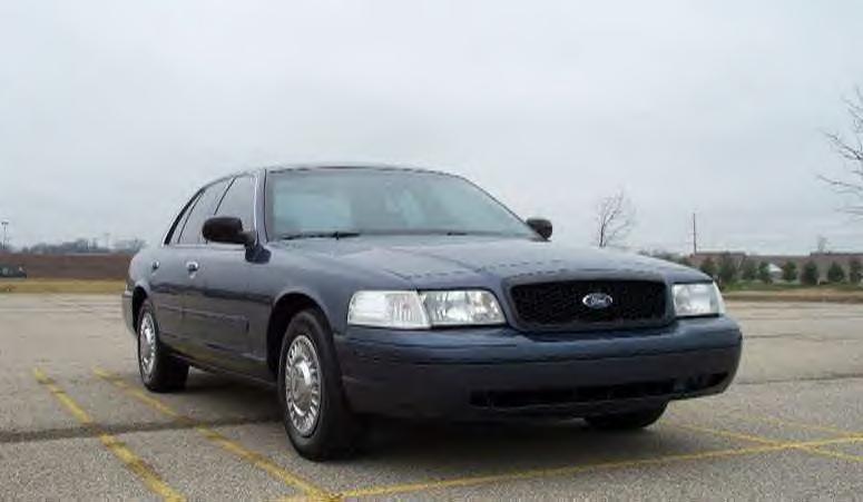 Dark blue Ford Crown Victoria sedan with A-pillar spotlight parked in an empty lot, front three-quarter view