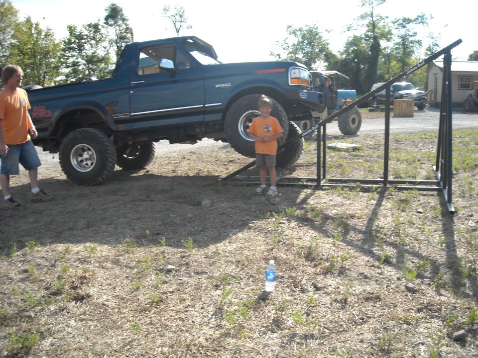 Blue lifted Ford Bronco on a ramp obstacle with a child and adult