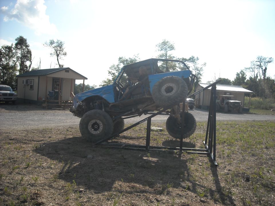 Blue stripped off-road rig climbing a steel ramp obstacle outdoors
