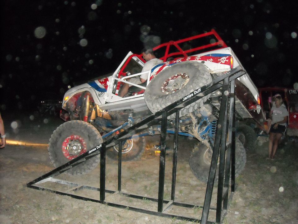 White off-road rig on a steel ramp obstacle at night