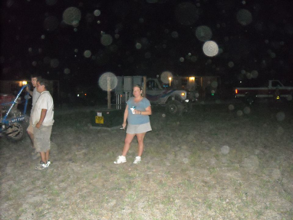 People standing in a field at night with off-road trucks parked behind them