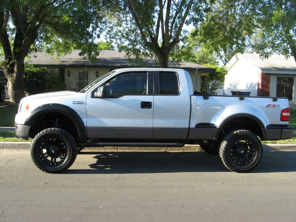 Silver lifted pickup truck with black fender flares and wheels parked on a street.