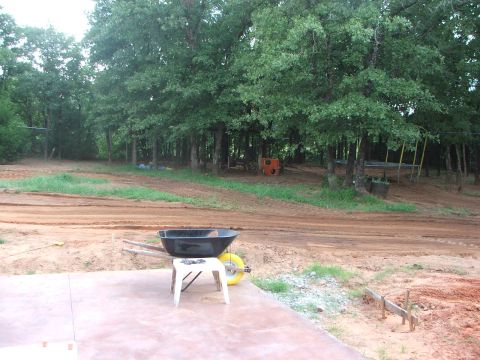 2005 Ford Mustang - A construction site with a wheelbarrow and a small white stool in the foreground, with trees and a dirt road in the background.