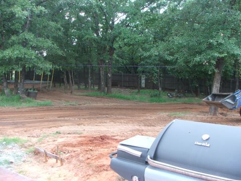 2005 Ford Mustang - A charcoal grill is in the foreground with a dirt road and trees in the background. A blue tractor with a front loader is visible on the ri…