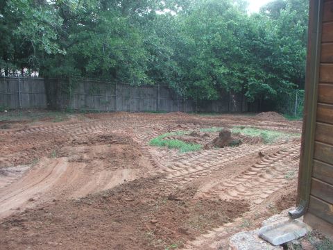 2005 Ford Mustang - A dirt lot with tire tracks from heavy machinery is shown with a wooden fence and trees in the background. A downspout from a wooden buildi…