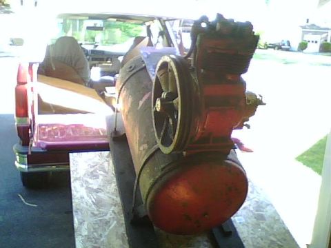 1995 Ford Bronco - A red air compressor is loaded into the bed of a red pickup truck. The air compressor has a large tank and a visible engine with a pulley.