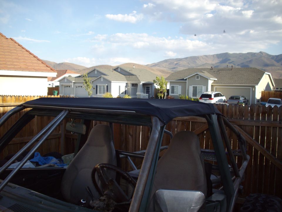 Interior of a custom off-road vehicle with a roll cage and dark top, suburban houses in background.