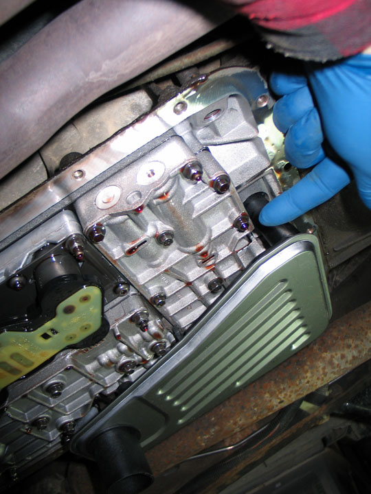 Close-up of a vehicle transmission pan with a new filter and red fluid.