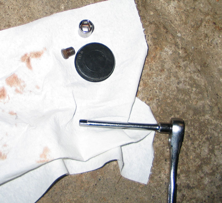 Socket wrench, socket, bolt, and cap on a paper towel with stains.