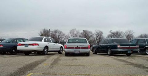 1988 Ford Crown Victoria - A white Ford Crown Victoria is seen from the rear, parked alongside other sedans in a lot.