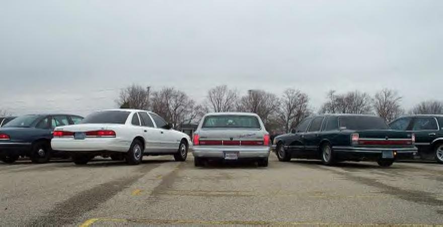 Row of full-size sedans parked rear-first, including a white Crown Victoria and silver Lincoln