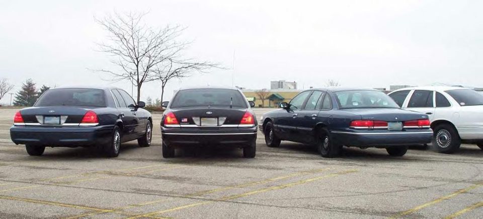 Four Ford Crown Victoria sedans lined up rear-first in an empty parking lot