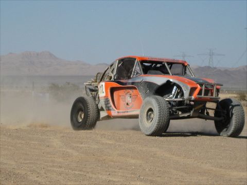1996 Ford Bronco - Off-road buggy races across a dusty desert landscape under a clear blue sky.