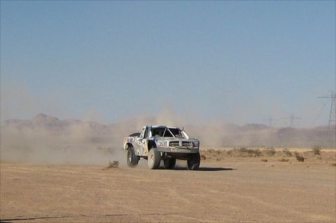 1996 Ford Bronco - A desert race truck speeds across a dusty, arid landscape under a clear blue sky.