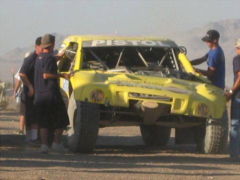 1996 Ford Bronco - A yellow off-road truck is being worked on by several people in a desert environment.