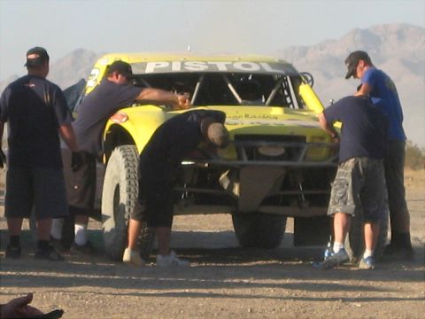 1996 Ford Bronco - Crew members attend to a yellow off-road racing truck with 'PISTOL' visible on the windshield.