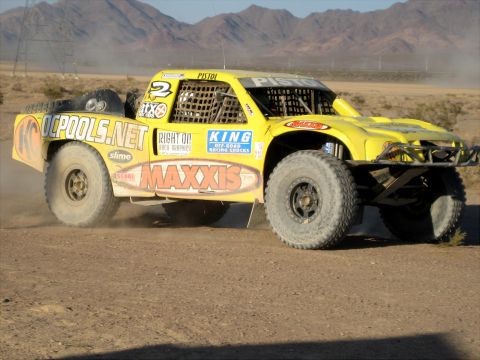 1996 Ford Bronco - A yellow off-road racing truck kicks up dust as it speeds across a desert landscape.