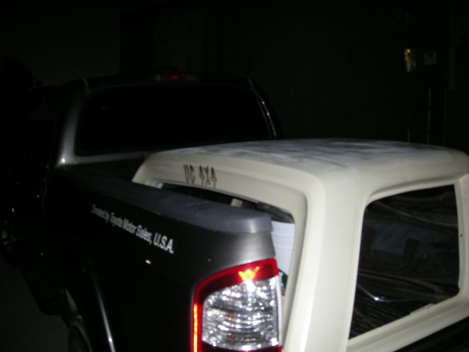 Rear view of a dark pickup truck bed carrying a white camper shell. Text on truck reads 'Distributed by Toyota Motor Sales, U.S.A.' and 'DC 4X4' on the shell