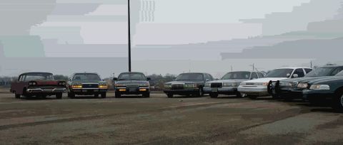 1988 Ford Crown Victoria - A collection of vehicles are lined up outdoors under an overcast sky.
