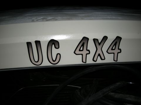 1991 Ford Bronco - A white vehicle displays a "UC 4X4" decal on its rear, with a dark interior visible beneath.
