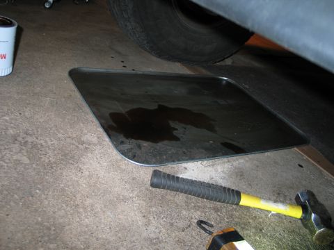 1994 Ford Bronco - Oil drain pan catching fluid under a vehicle, with a sledgehammer on the floor.