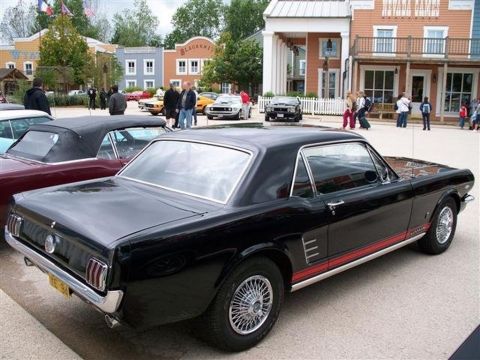 1991 Ford Crown Victoria - A black 1965 Ford Mustang coupe is parked in front of a western-themed town facade.