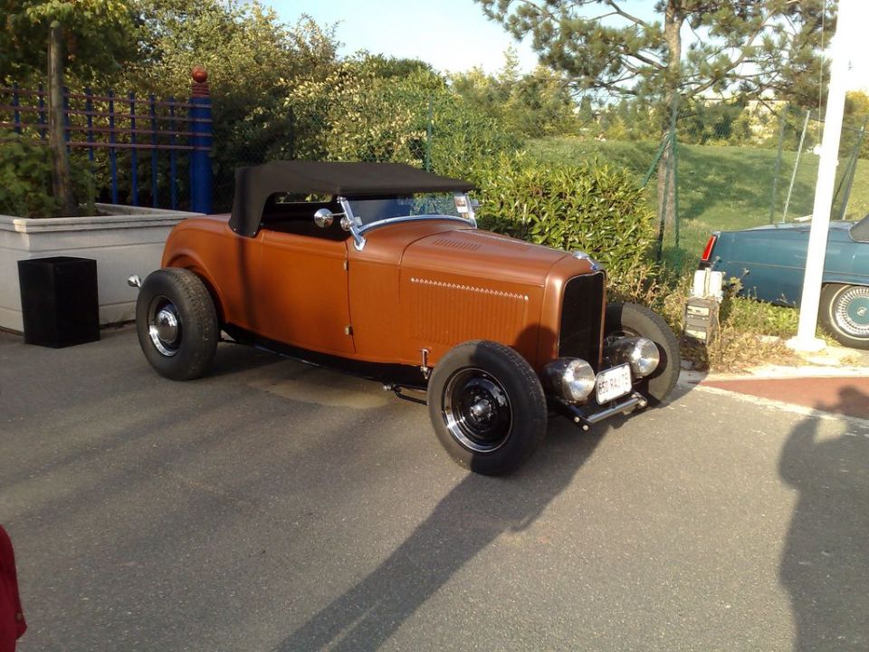 Brown hot rod convertible with black top parked outside. Another car is visible to the right