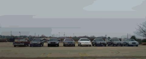 1988 Ford Crown Victoria - A group of Ford Crown Victorias and other sedans are lined up in a parking lot on an overcast day.