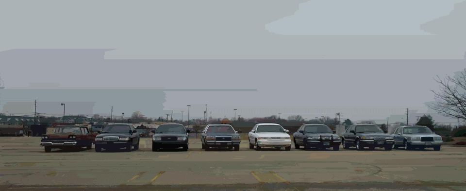 Eight full-size sedans lined up facing camera in an empty parking lot