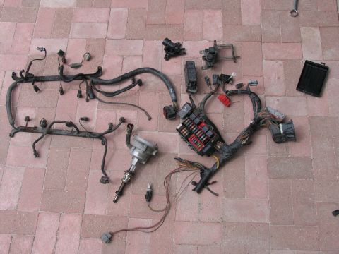 1984 Ford Bronco - Various engine electrical components, including a wiring harness and fuse box, are spread out on a tiled surface.