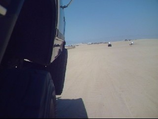 1984 Ford Bronco - Multiple off-road vehicles are seen on a sandy beach under a clear blue sky. Supermotors.net logo is present.