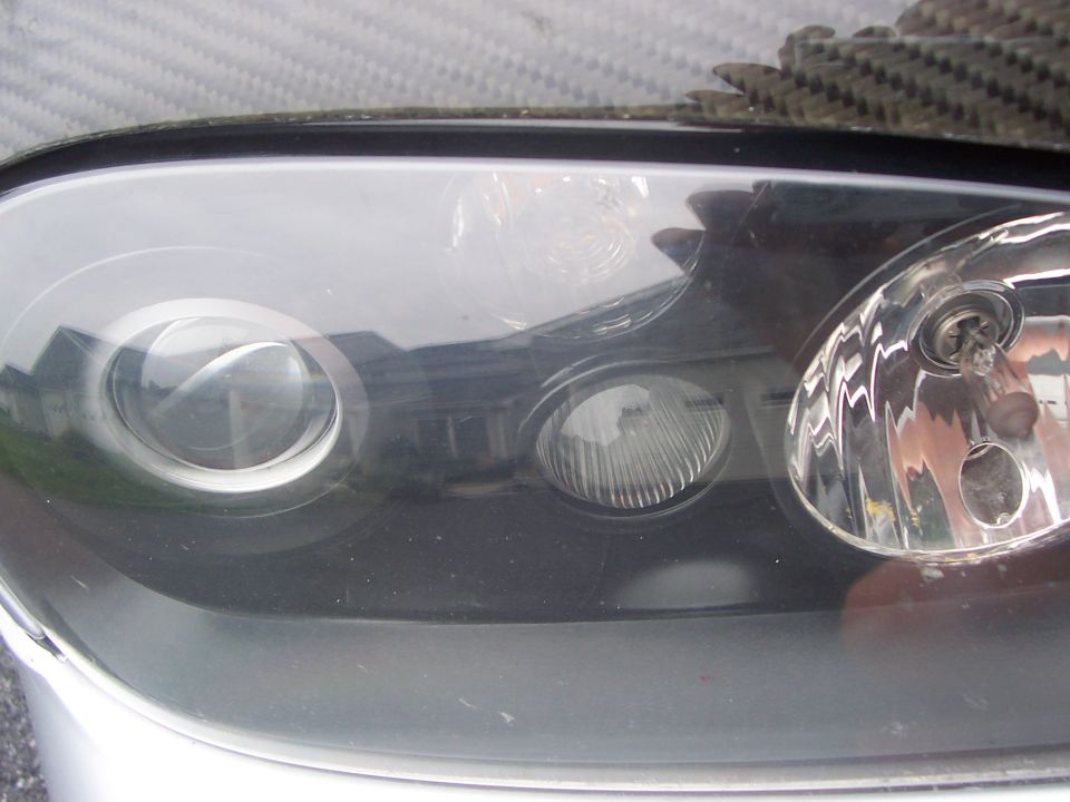 Close-up of a car headlight assembly with multiple bulbs and a carbon fiber trim piece above