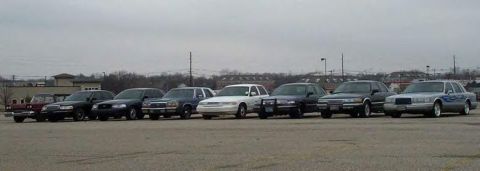 1988 Ford Crown Victoria - A group of sedans are lined up in a parking lot under an overcast sky.