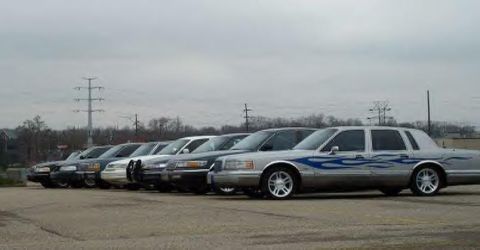 1988 Ford Crown Victoria - A row of sedans, including one with custom flame decals, are parked outdoors on a cloudy day.