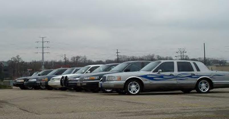 Silver Lincoln Town Car with blue flame graphics leading a line of parked sedans
