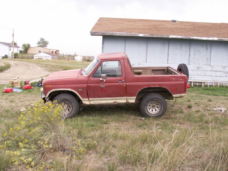 Red Ford Bronco parked in grassy area next to a building. Spare tire mounted on rear