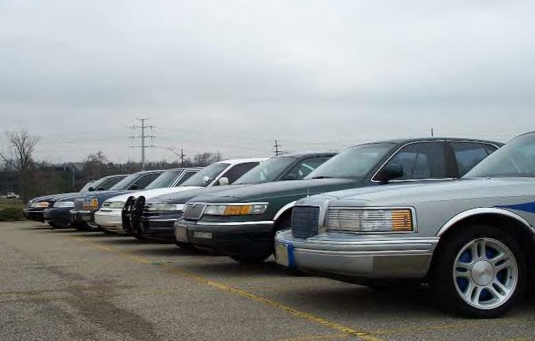 Low angle down a lineup of full-size sedans led by a silver Lincoln Town Car
