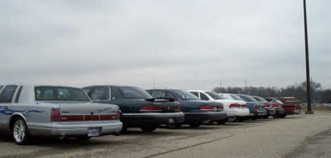 1988 Ford Crown Victoria - A row of sedans are parked in a lot under an overcast sky.