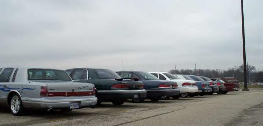 Row of parked full-size Ford/Lincoln sedans seen from rear three-quarter on an overcast day