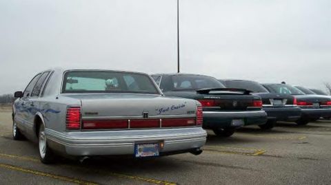 1988 Ford Crown Victoria - Several sedans are parked in a lot under an overcast sky. The closest car has blue flame decals.