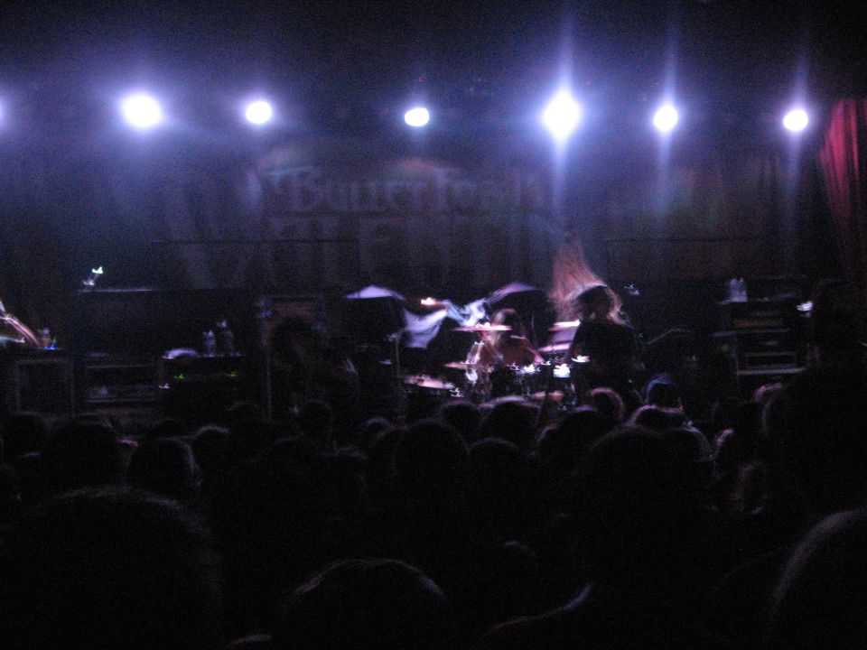 Dark concert stage with drummer and crowd silhouettes