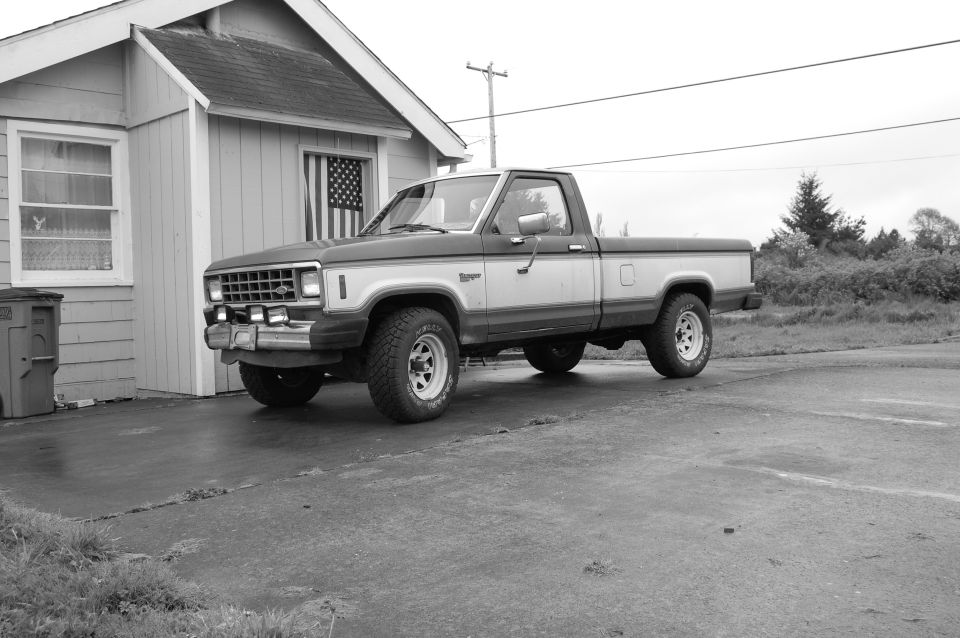 1985 Ford Ranger pickup truck, black and white, parked in front of a house.
