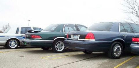 1988 Ford Crown Victoria - A trio of Ford Crown Victorias are lined up in a parking lot, showing their rear ends.