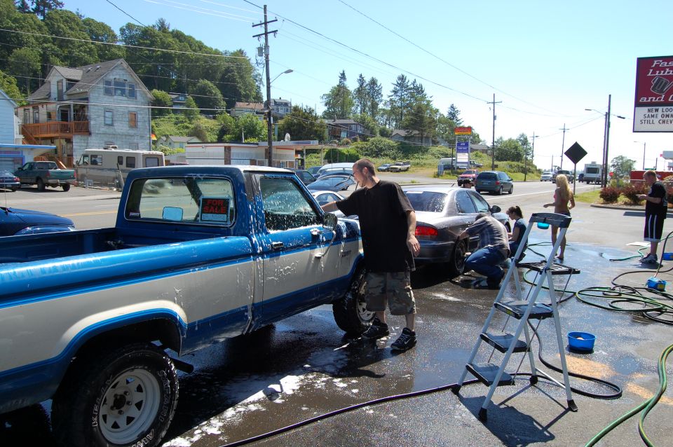 Blue and silver pickup truck being washed with soap suds at outdoor car wash event