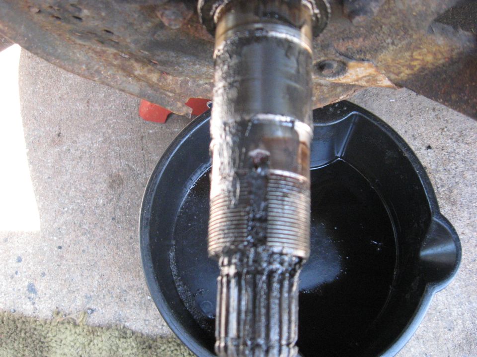 Splined axle shaft dripping fluid into a drain pan, with rusted brake drum of a 1994 Ford Bronco.