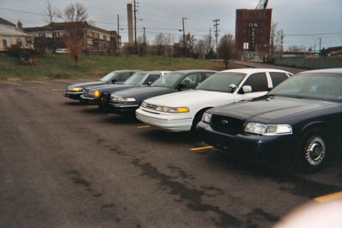 1988 Ford Crown Victoria - Multiple Ford Crown Victoria police cars are lined up in a parking lot under an overcast sky.