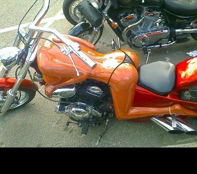 1988 Mercury Grand Marquis - A custom motorcycle with a body painted to resemble a woman in a bikini. The motorcycle is orange and red with chrome accents and dual exha…