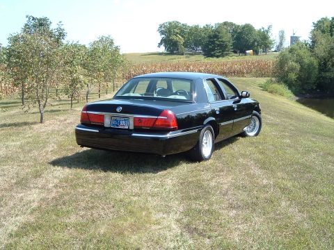 2001 Mercury Grand Marquis - A black 2001 Mercury Grand Marquis is parked on a grassy hill next to a field of corn and trees. The rear driver's side of the car is visib…